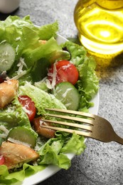 Photo of Eating delicious salad with chicken, cheese and vegetables at grey table, closeup