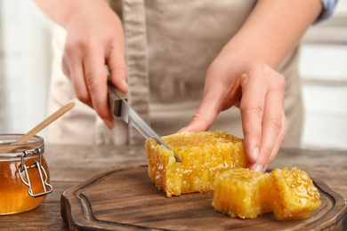 Photo of Woman cutting fresh honeycomb at table, closeup