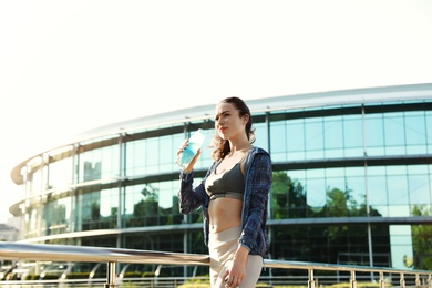 Photo of Young woman drinking water after running in city. Sports hydration