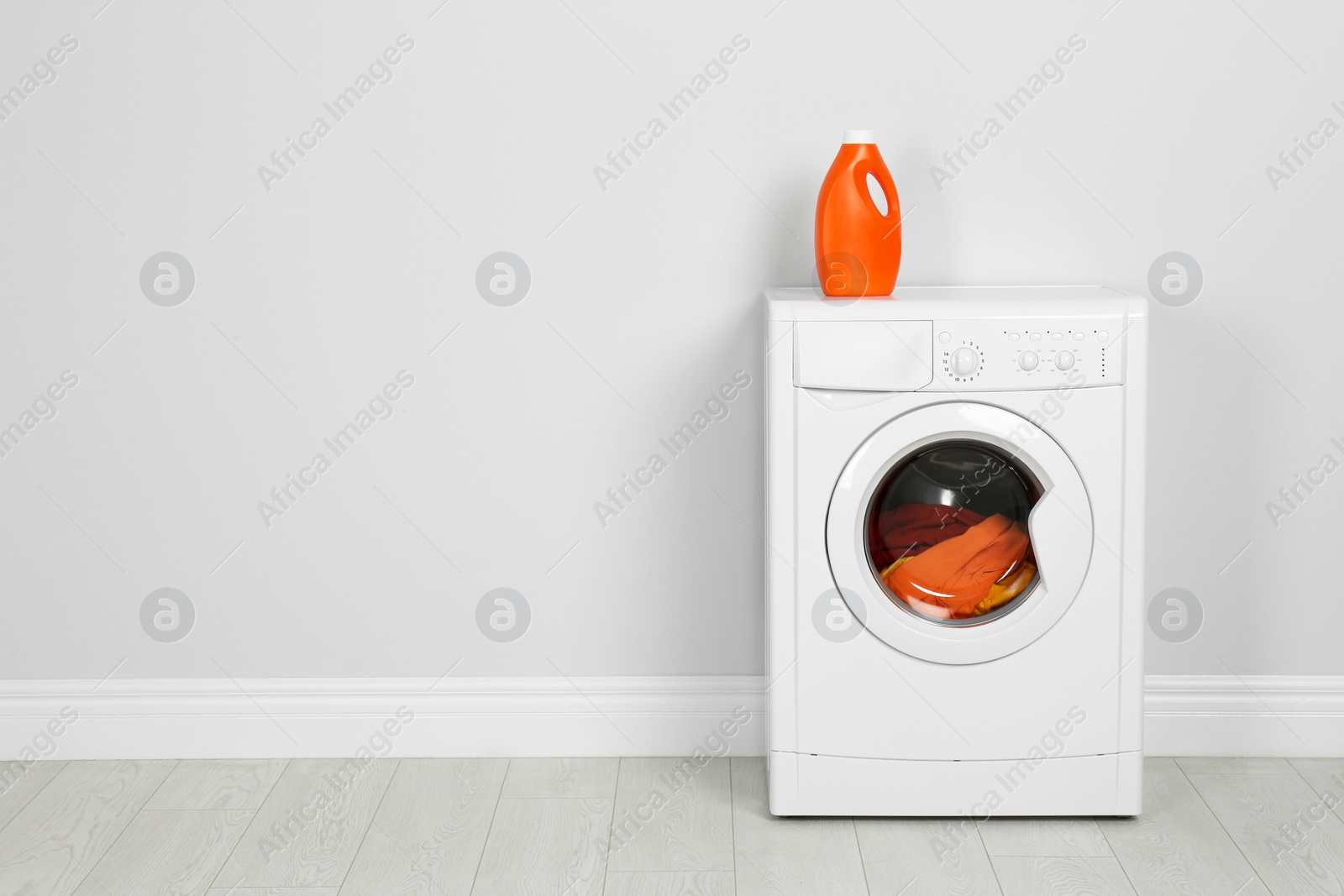 Photo of Modern washing machine with laundry and detergent near white wall. Space for text
