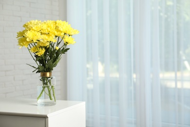 Photo of Vase with beautiful yellow chrysanthemum flowers on table near window indoors, space for text. Stylish element of interior design