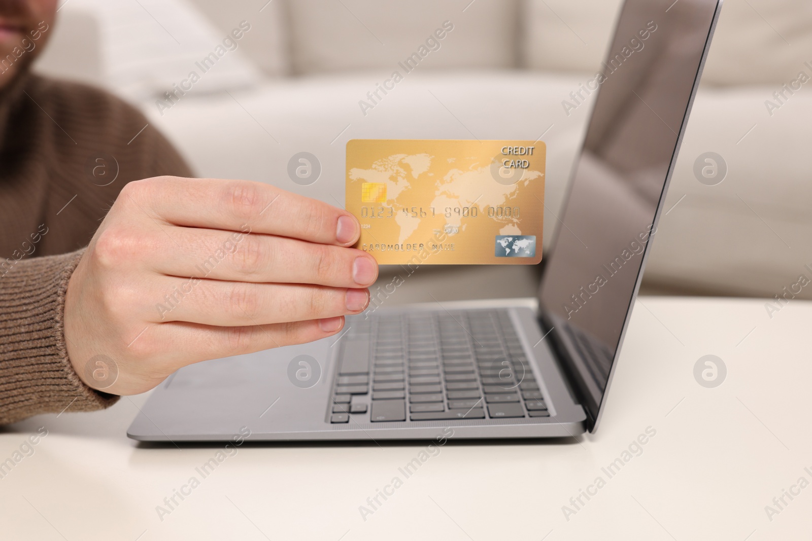 Photo of Man with credit card using laptop for online shopping at white table indoors, closeup