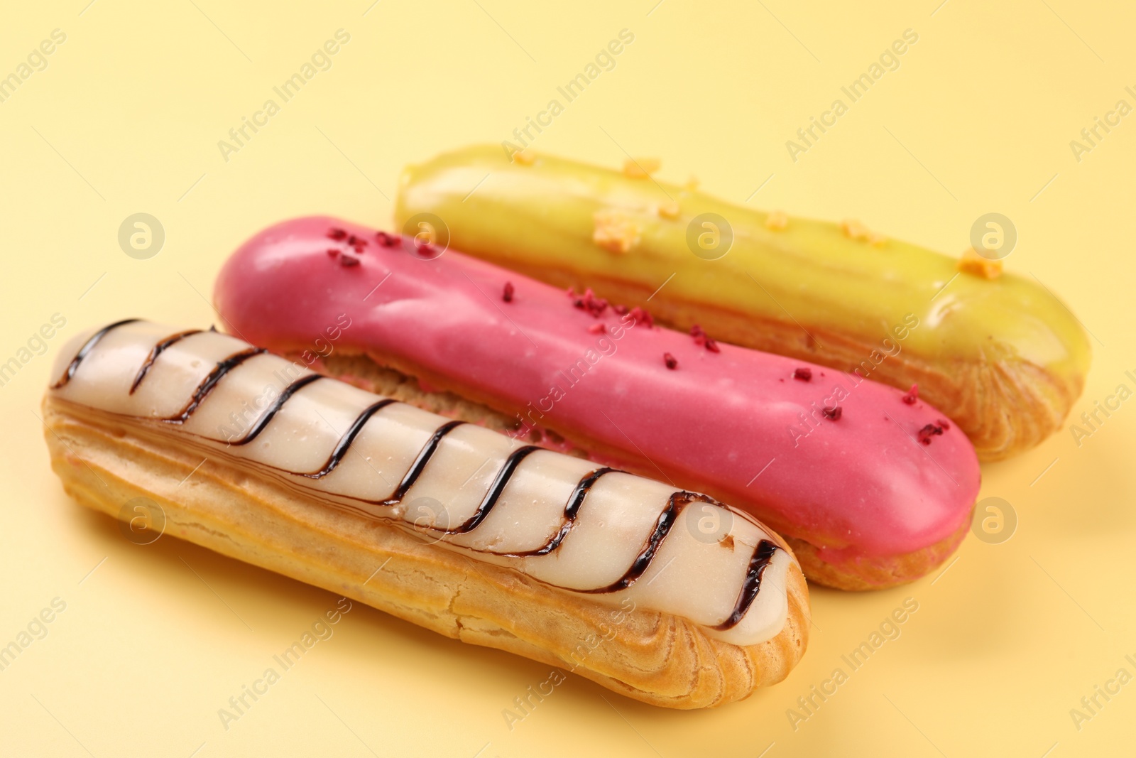 Photo of Delicious eclairs covered with glaze on yellow background