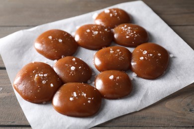 Tasty caramel candies and salt on wooden table