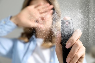 Image of Young woman covering eyes with hand and using pepper spray at home