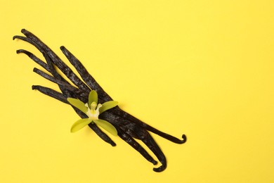 Photo of Vanilla pods and beautiful flower on yellow background, top view. Space for text
