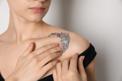 Photo of Woman applying cream onto tattoo on her skin against light background, closeup