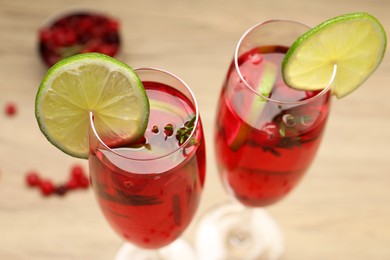 Photo of Tasty cranberry cocktail with rosemary and lime in glasses on beige table, closeup