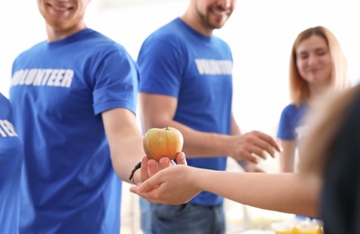 Volunteer giving apple to poor person, closeup