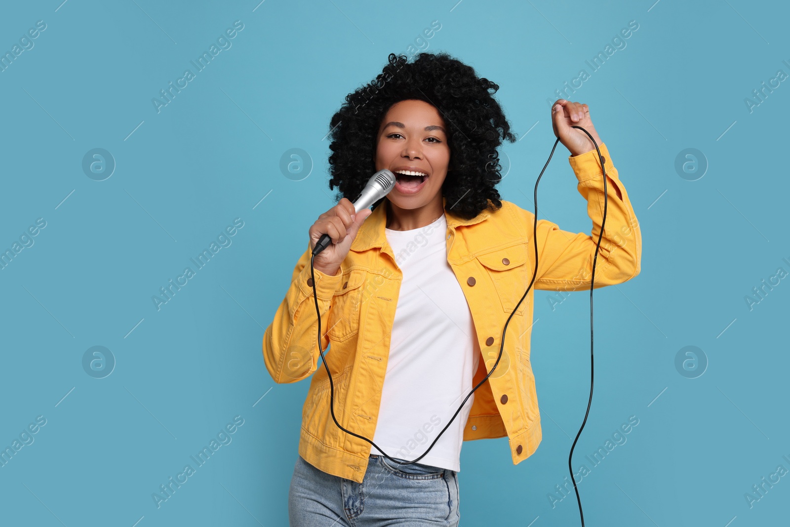 Photo of Beautiful woman with microphone singing on light blue background