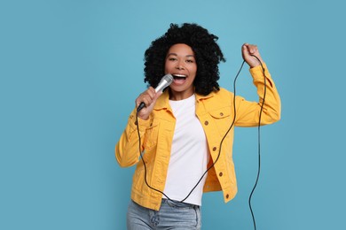 Beautiful woman with microphone singing on light blue background