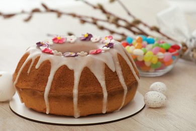 Photo of Delicious Easter cake decorated with sprinkles near eggs and candies on white wooden table, closeup
