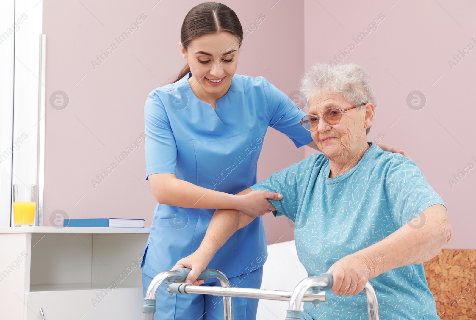 Photo of Nurse assisting senior woman with walker in hospital ward