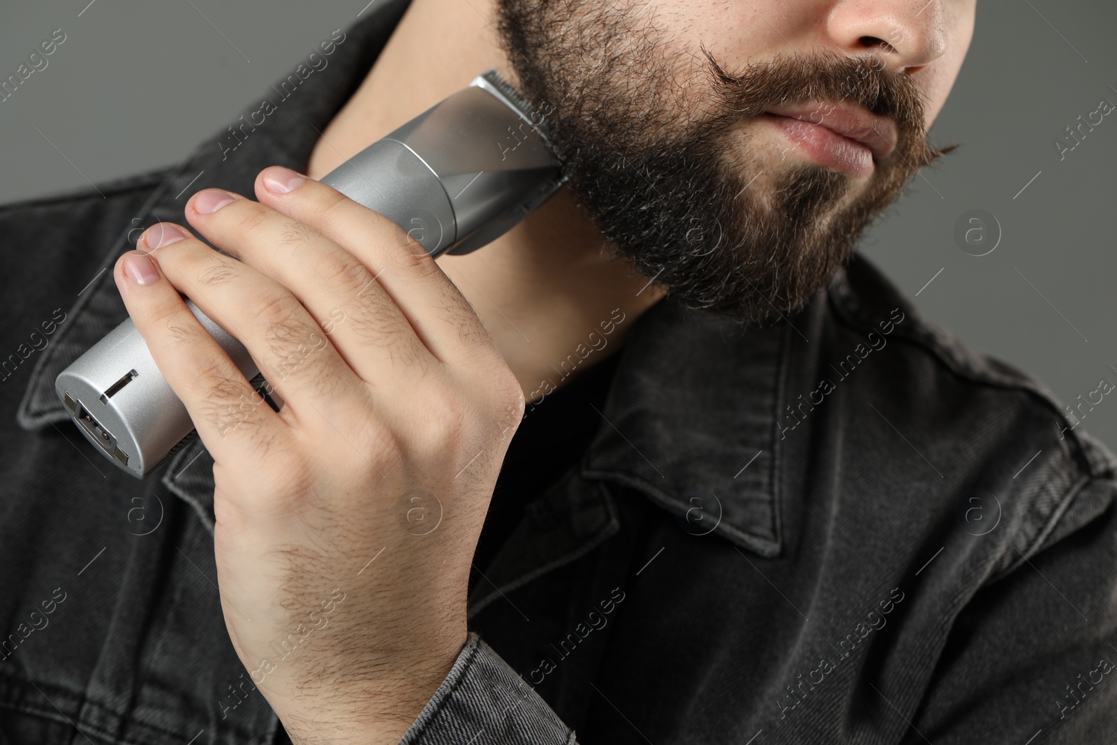 Photo of Handsome young man trimming beard on grey background