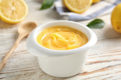 Photo of Delicious lemon curd in bowl on white wooden table, closeup