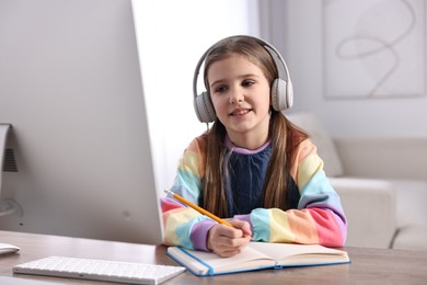 Photo of E-learning. Cute girl taking notes during online lesson at table indoors