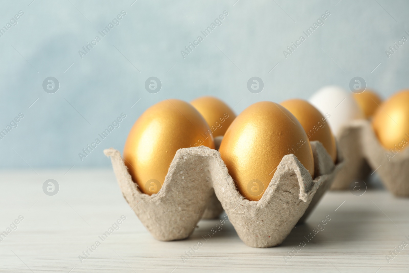 Photo of Carton with golden eggs on white wooden table, closeup