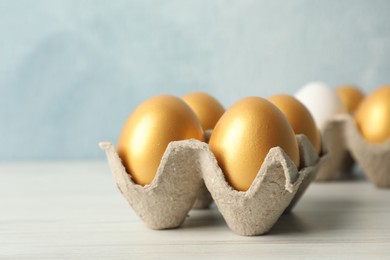 Photo of Carton with golden eggs on white wooden table, closeup
