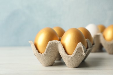 Carton with golden eggs on white wooden table, closeup