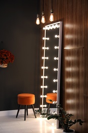 Image of Full length dressing mirror with lamps and stool in stylish room interior