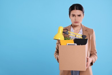 Photo of Upset unemployed woman with box of personal office belongings on light blue background. Space for text