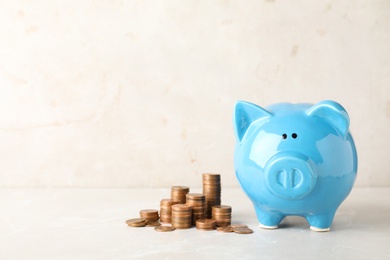 Photo of Ceramic piggy bank and many coins on table against light background. Space for text