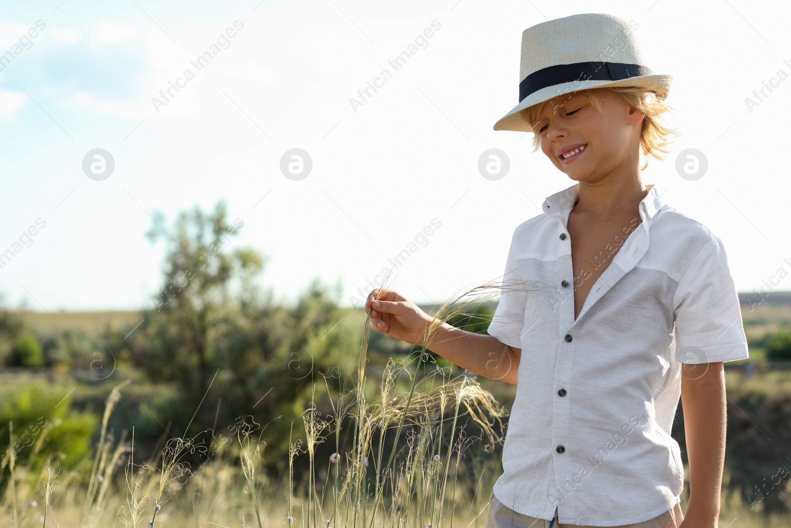 Photo of Cute little boy wearing stylish hat outdoors, space for text. Child spending time in nature