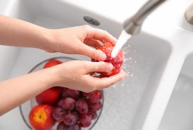 Photo of Woman washing fresh nectarine in kitchen sink, top view