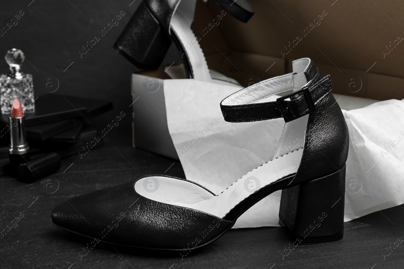 Photo of Stylish female shoes and cardboard box on black stone table, closeup