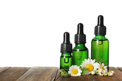 Chamomile flowers and cosmetic bottles of essential oil on wooden table against white background. Space for text