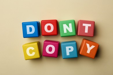 Photo of Colorful cubes with words Don't Copy on beige background, flat lay. Plagiarism concept