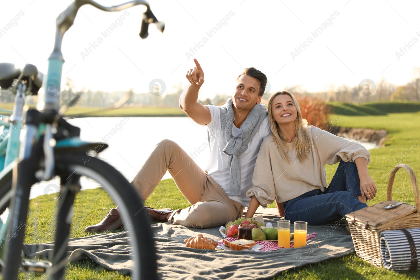 Photo of Happy young couple having picnic near lake on sunny day