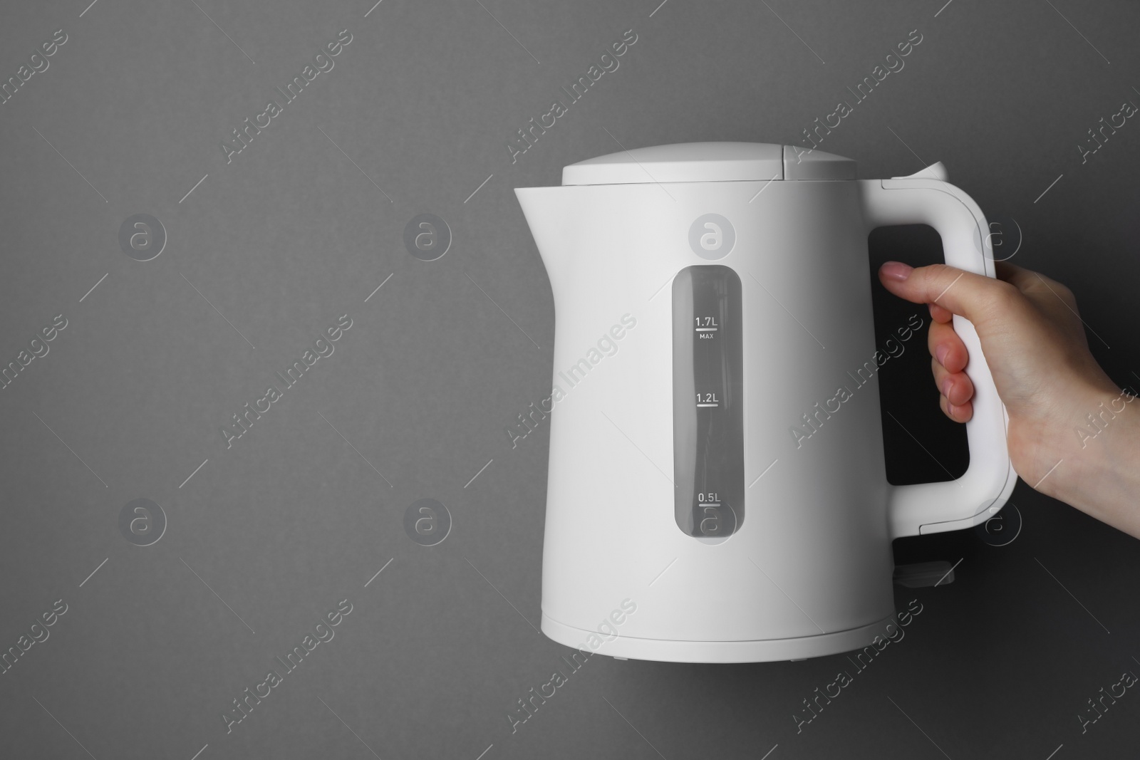 Photo of Woman holding modern electric kettle on grey background, closeup. Space for text