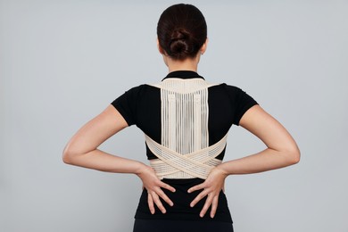 Woman with orthopedic corset on grey background, back view