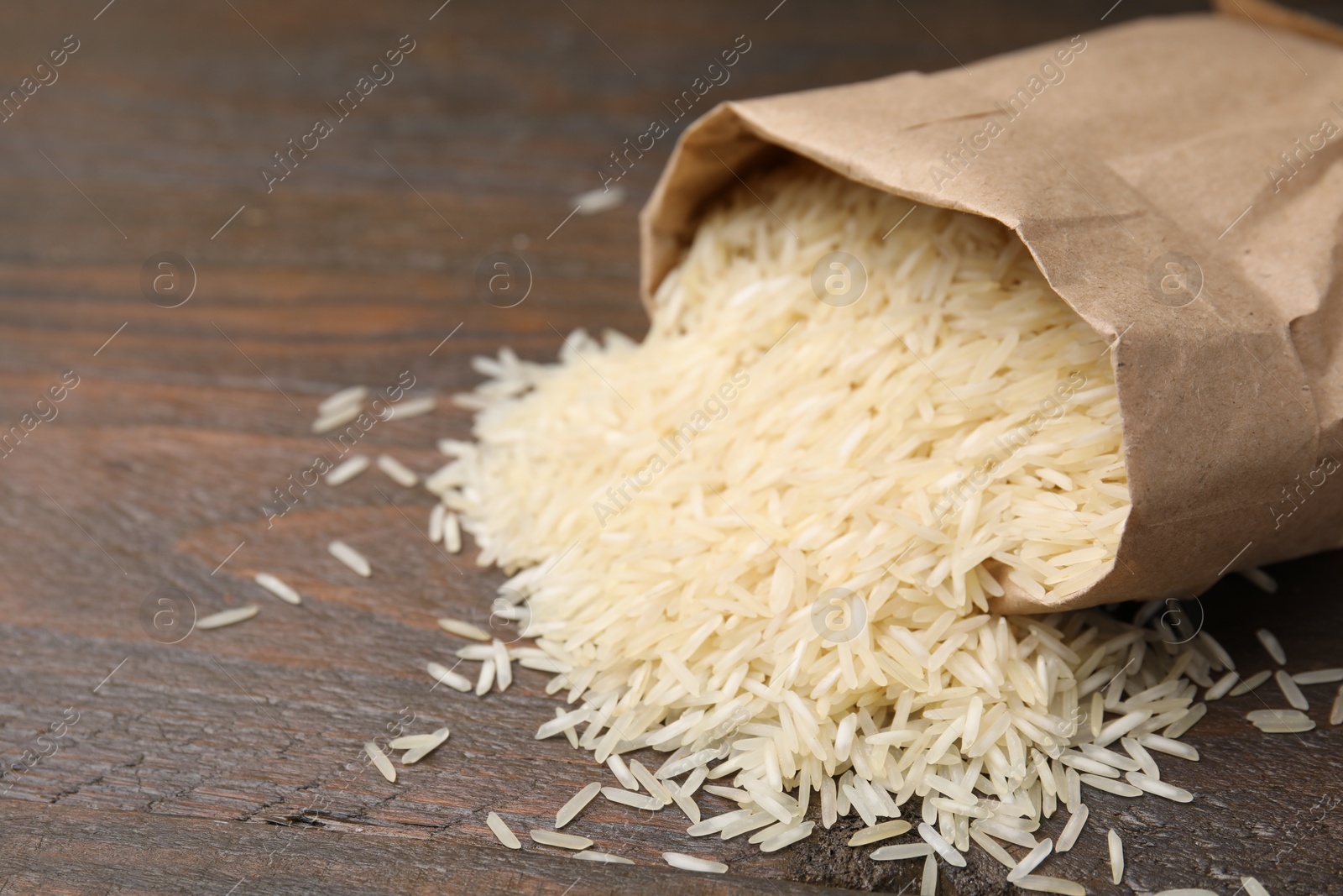 Photo of Overturned paper bag with raw rice on wooden table, closeup. Space for text