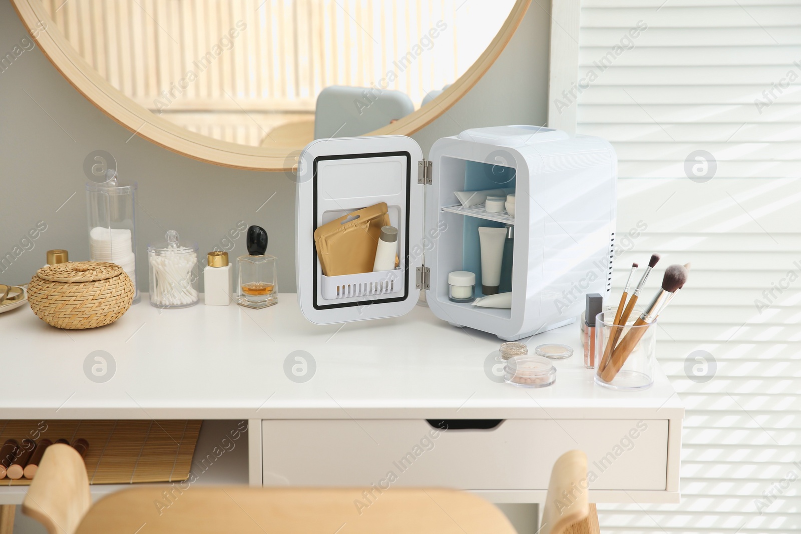 Photo of Cosmetics refrigerator and skin care products on white vanity table indoors