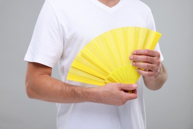 Photo of Man holding hand fan on light grey background, closeup