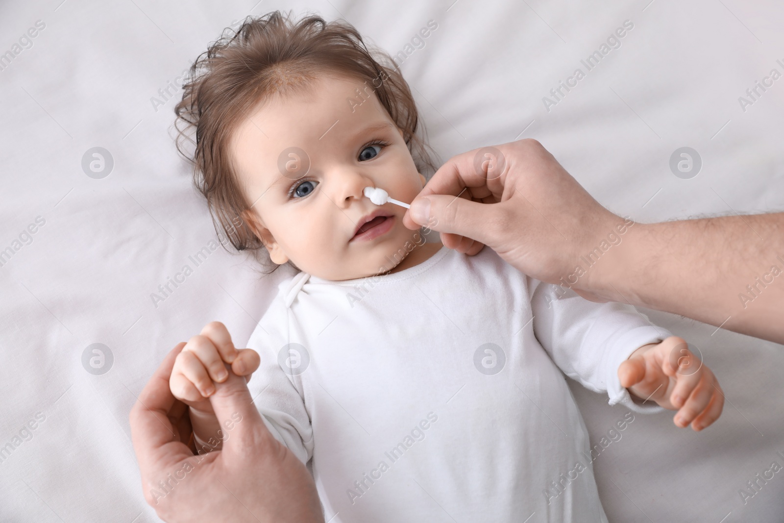 Photo of Father cleaning nose of his baby with cotton bud on bed, top view