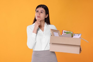 Photo of Thoughtful unemployed woman with box of personal office belongings on orange background