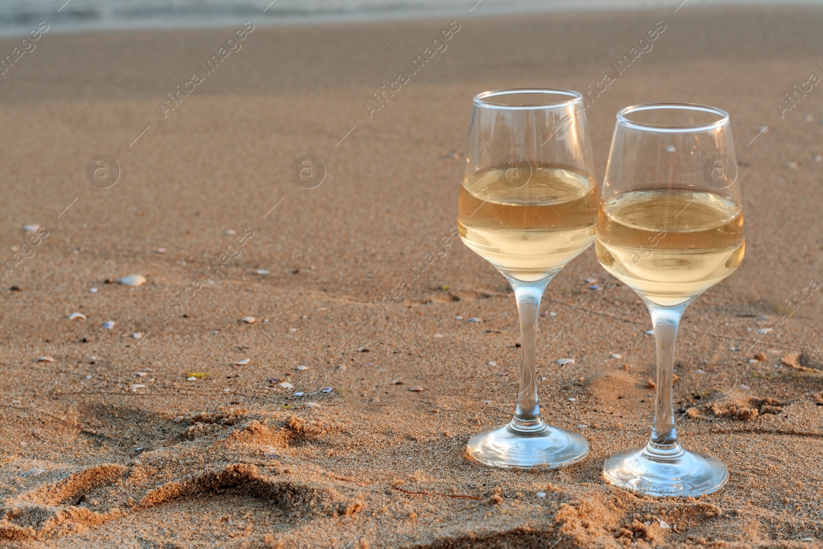 Photo of Glasses of tasty wine on sandy beach, space for text