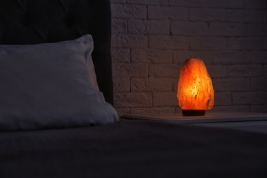 Photo of Himalayan salt lamp glowing on bedside table in dark room
