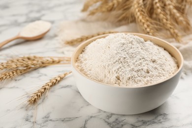 Photo of Bowl of flour and wheat ears on white marble table