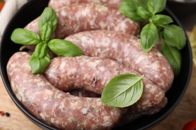 Raw homemade sausages and basil leaves in bowl on table, closeup