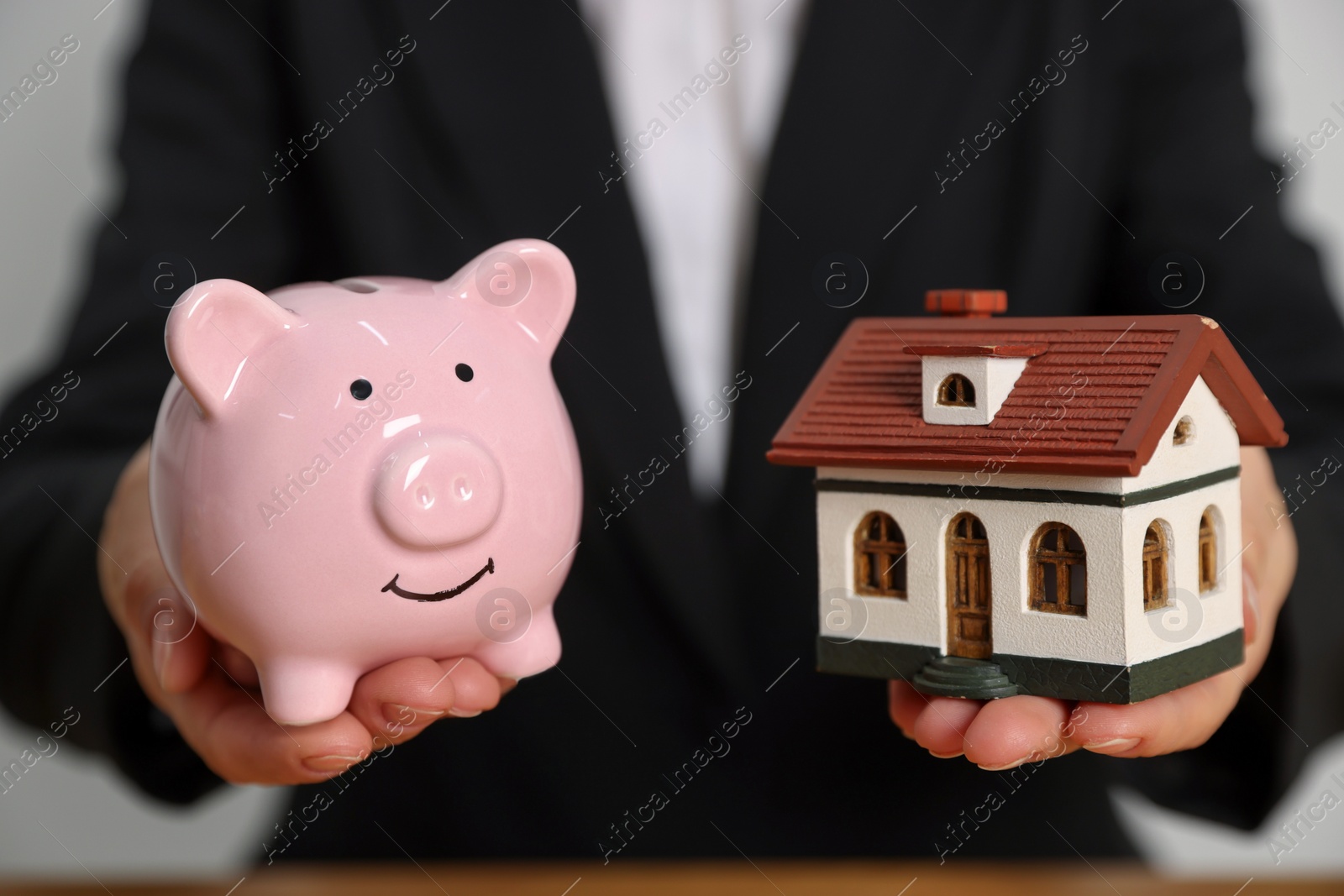 Photo of Woman holding piggy bank and little house model on light grey background, closeup