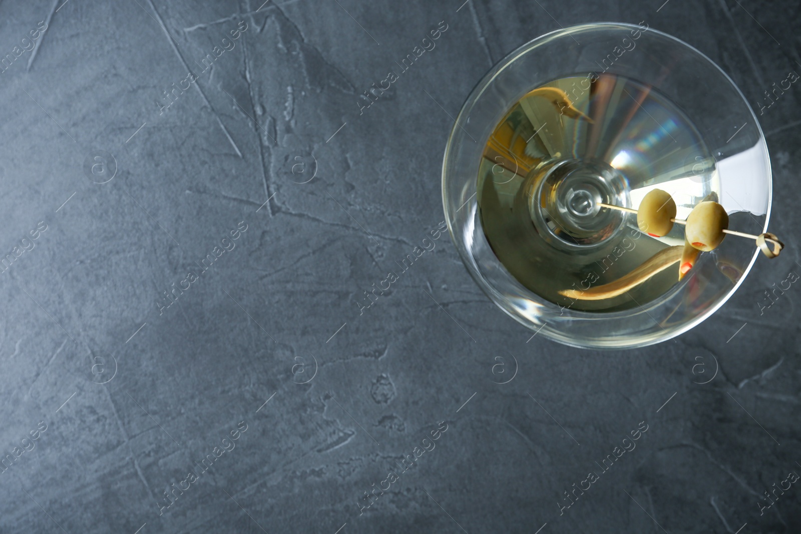 Photo of Glass of Classic Dry Martini with olives on dark grey table, top view. Space for text
