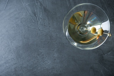 Photo of Glass of Classic Dry Martini with olives on dark grey table, top view. Space for text