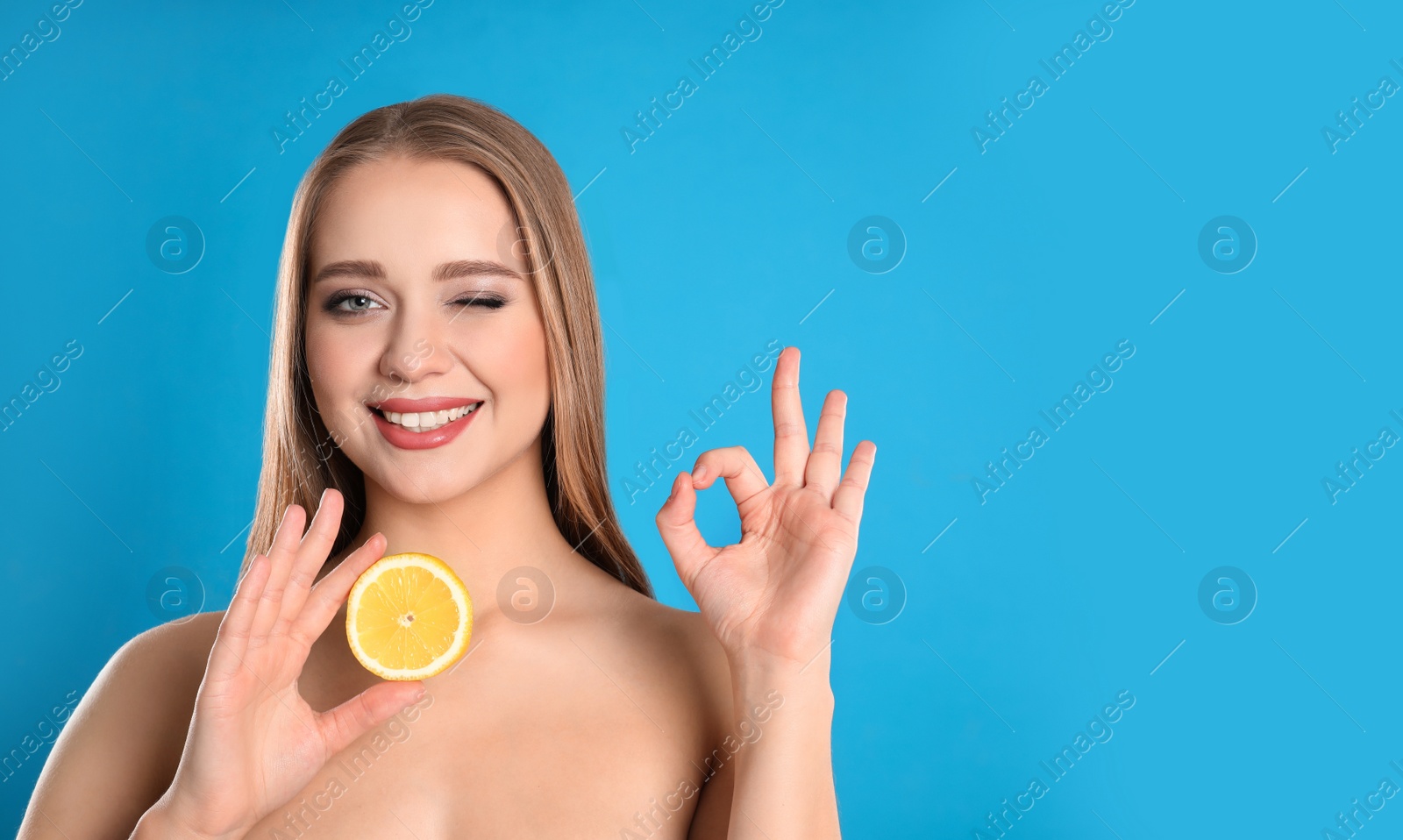 Photo of Young woman with cut lemon on blue background. Vitamin rich food