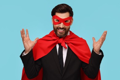 Photo of Businessman wearing red superhero cape and mask on light blue background