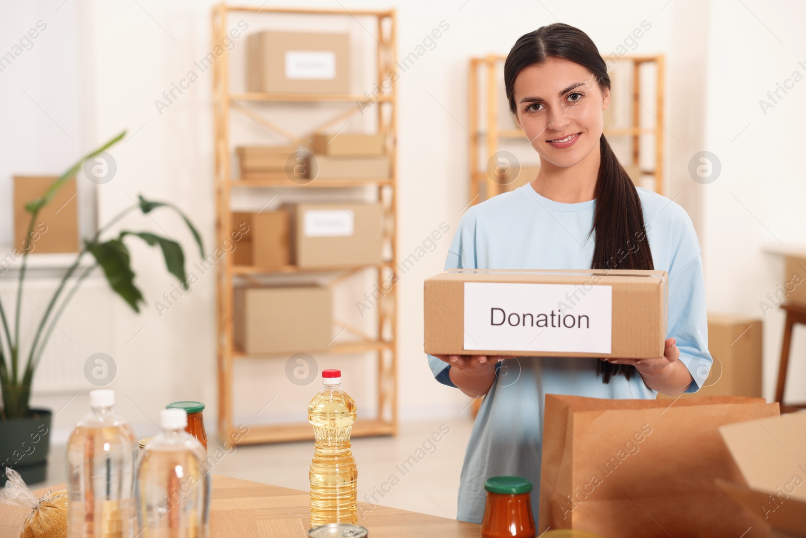 Photo of Volunteer with donation box and food products at table in warehouse