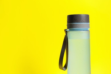 Photo of Stylish closed bottle with water drops on yellow background, closeup. Space for text